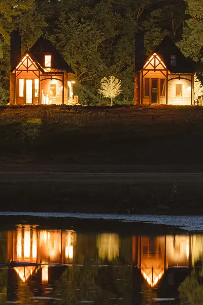 Four cabins lit up at night, reflected in water