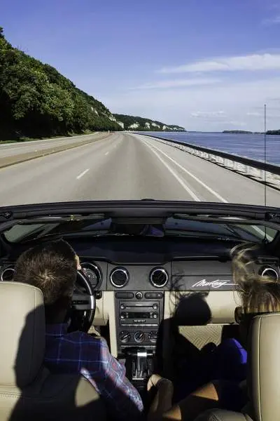 Two people driving in a roofless car down a road