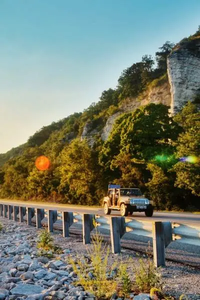 The sunrise shining over water and a car driving down road beside it