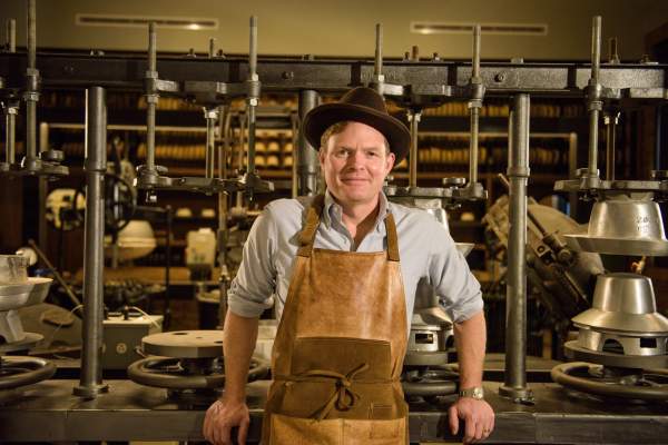 A man standing in front of hat making machines